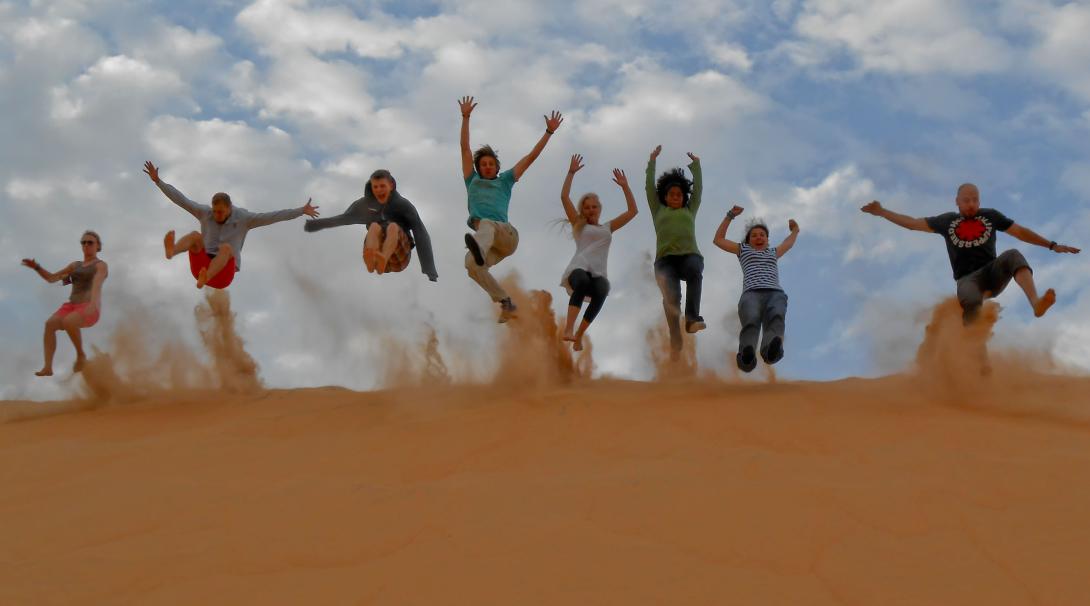 Projects Abroad volunteers enjoying their French Language Team Trip in Senegal Volunteers jumping on the hill of the dunes in Senegal shooting sand into the air for an epic photo